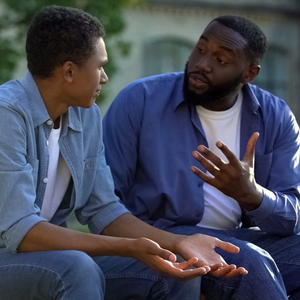 Father arguing teenage son sitting on campus bench, puberty age