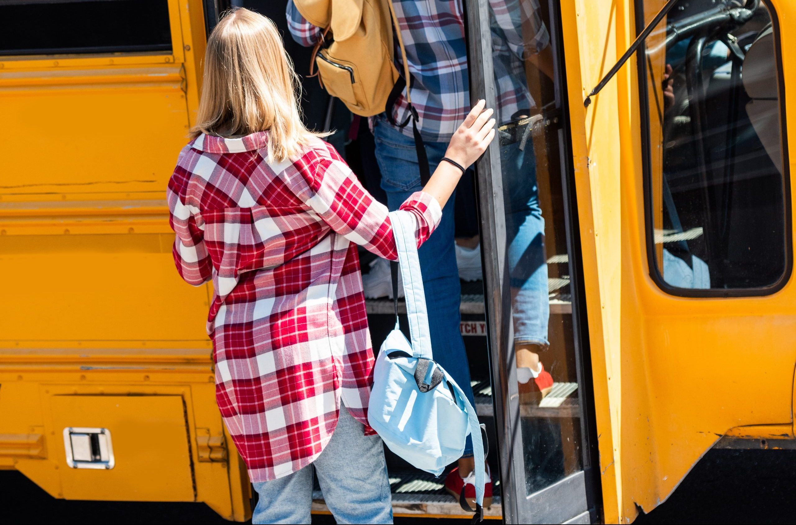 rear view of teen students walking into school bus
