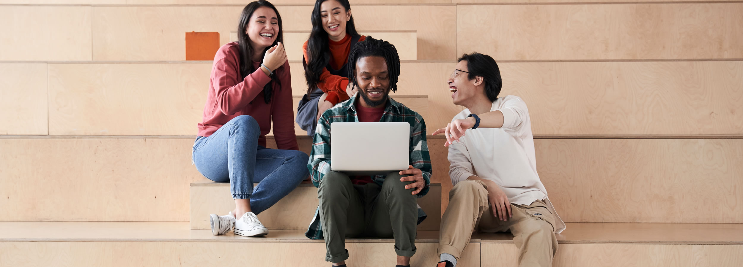 4 teens sitting together viewing a laptop and laughing